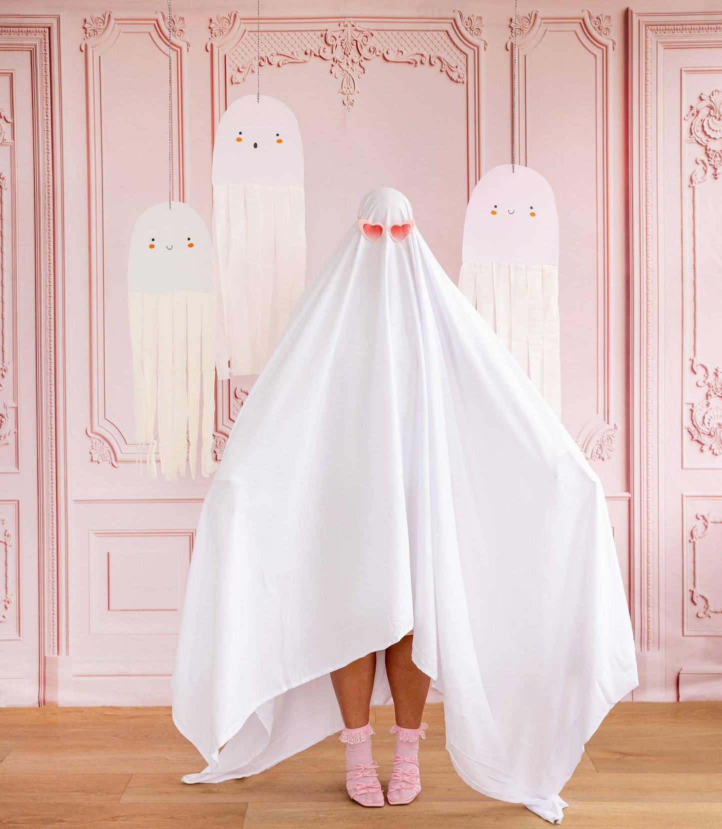 Person wearing a ghost costume with pink shoes in a room with decorative pink walls.