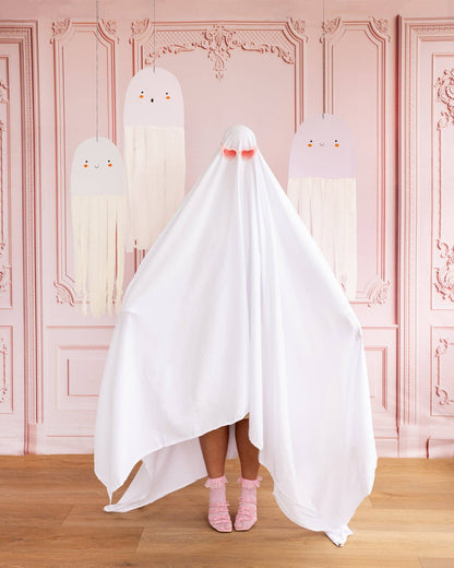 Person wearing a white ghost costume with pink shoes in front of a decorative pink wall with hanging ghost decorations.