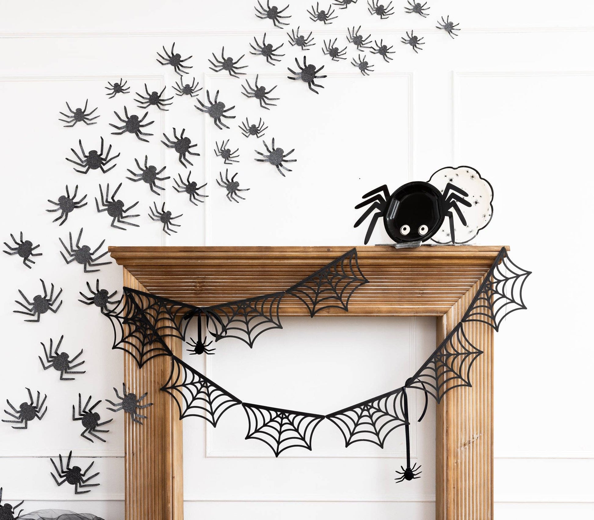 Halloween decorations including a spider web bunting and black glittered spiders on a white wall.