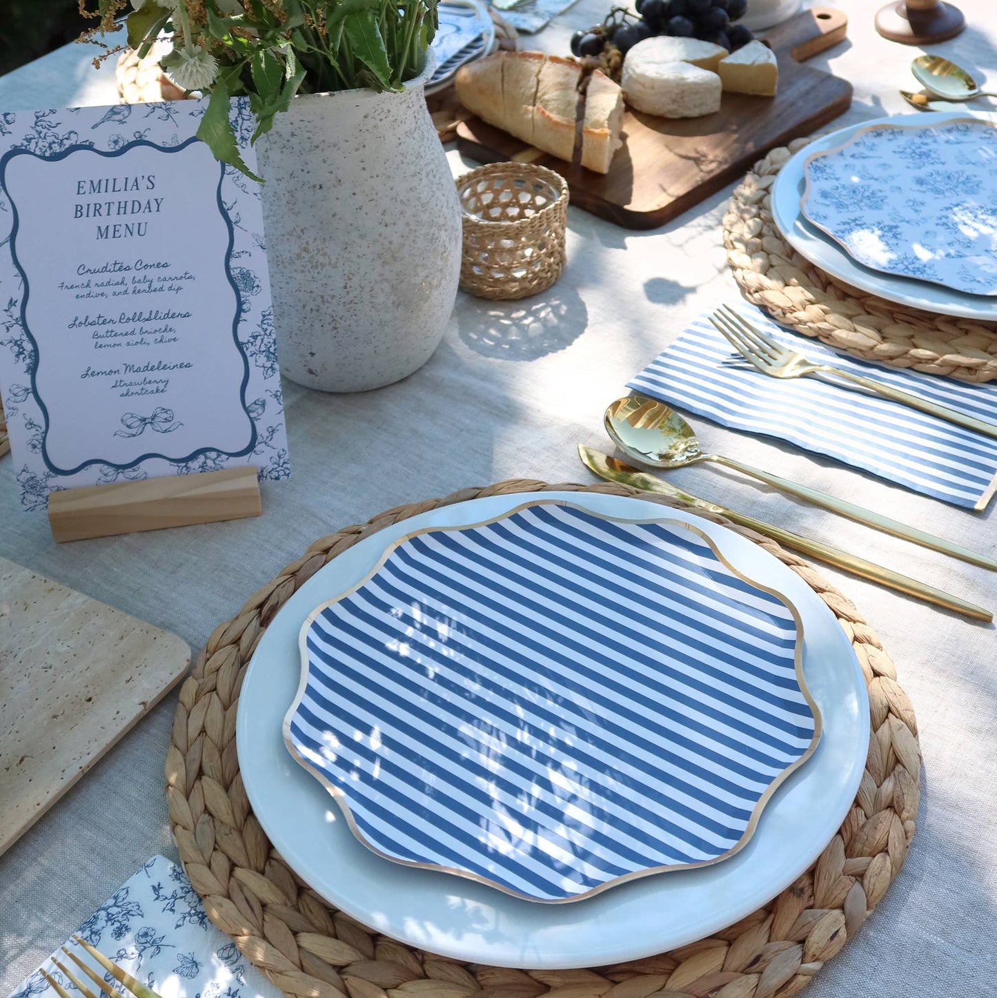 Set table with blue and white striped plates, gold cutlery, and a birthday menu card.