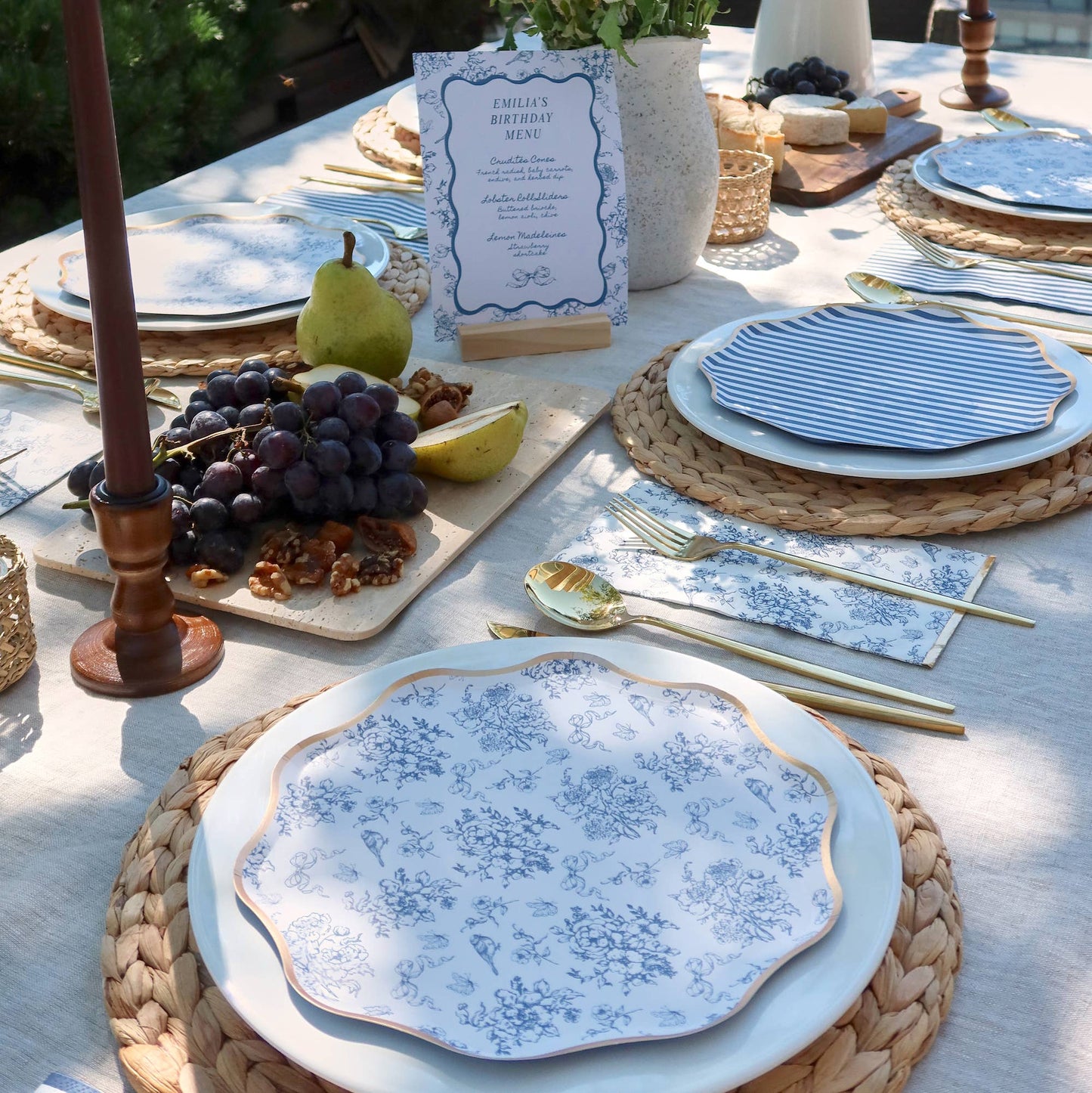 Elegant outdoor table setting with blue and white plates, cutlery, and decorative elements.