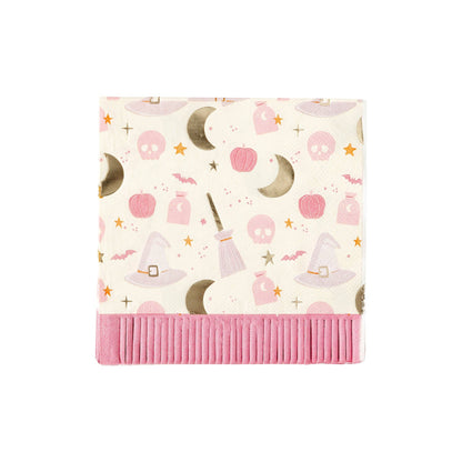 White beverage napkins with a pink and silver foil Halloween-themed pattern featuring skulls, pumpkins, moons, witch's hats, and brooms with a pink fringe trim.