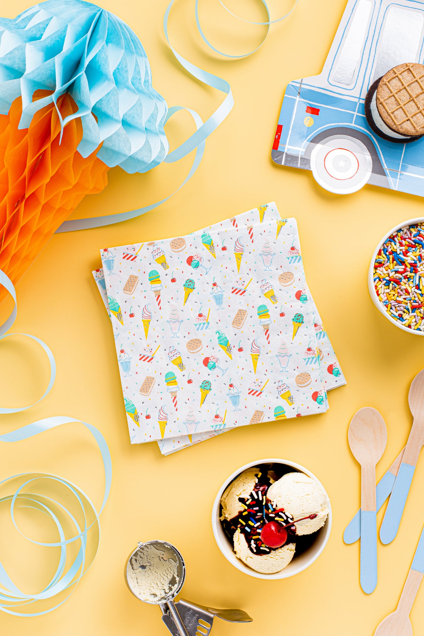 Colorful ice cream-themed paper napkins on a yellow background with party supplies.