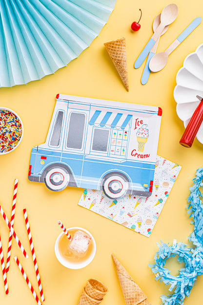 A flat-lay of light blue and white ice cream truck themed party supplies on a bright yellow background, including printed napkins, paper fans, straws, spoons, cones, and a small cup.