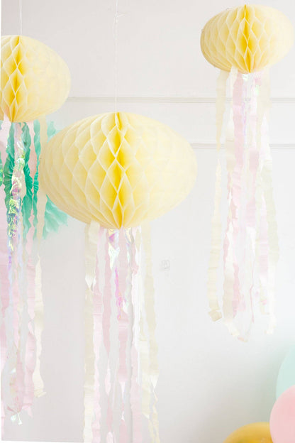 A set of honeycomb jellyfish decorations in yellow, with pink iridescent streamers, designed for party decor.
