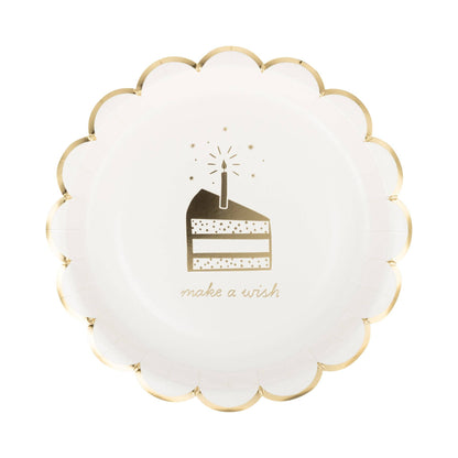 A round white paper party plate with a scalloped gold rim, featuring a gold illustration of a birthday cake slice with a lit candle and the words 'make a wish' printed below.
