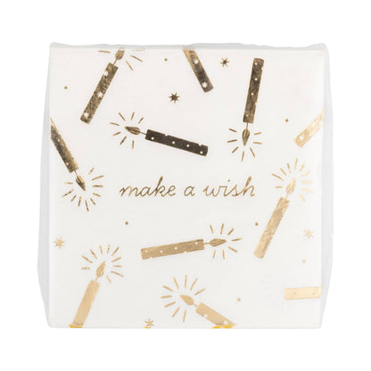A square white paper napkin featuring a gold foil print of sparklers, stars, and the phrase 'make a wish' in elegant script.