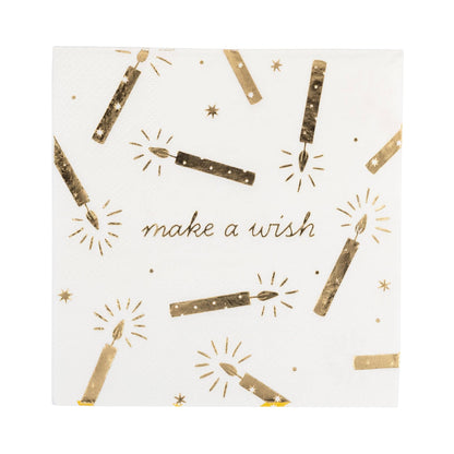 A square white paper napkin featuring a gold foil print of birthday candles, sparkles, and the words 'make a wish' in gold script.