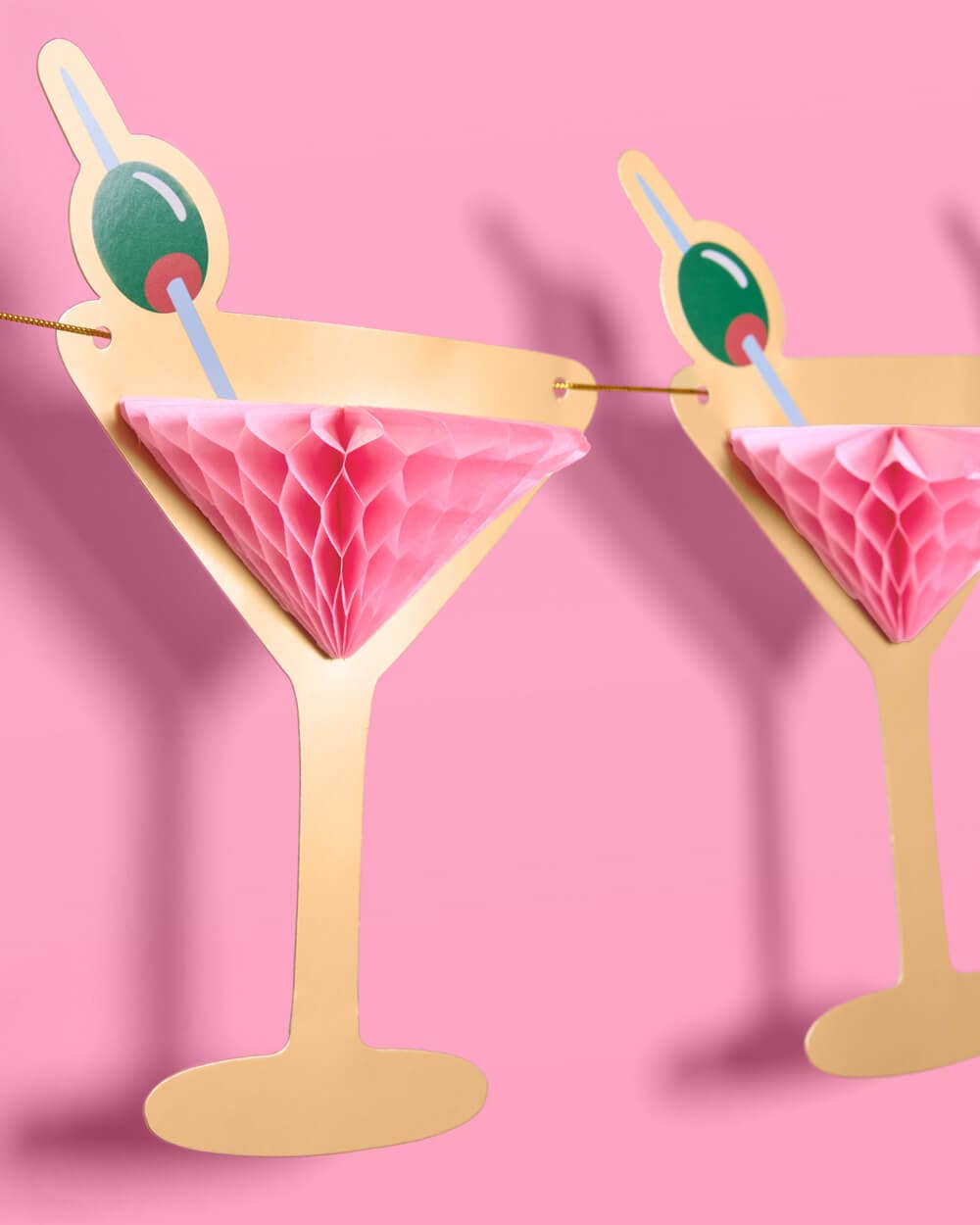 Decorative paper cocktail with pink drink and green olive on a pink background
