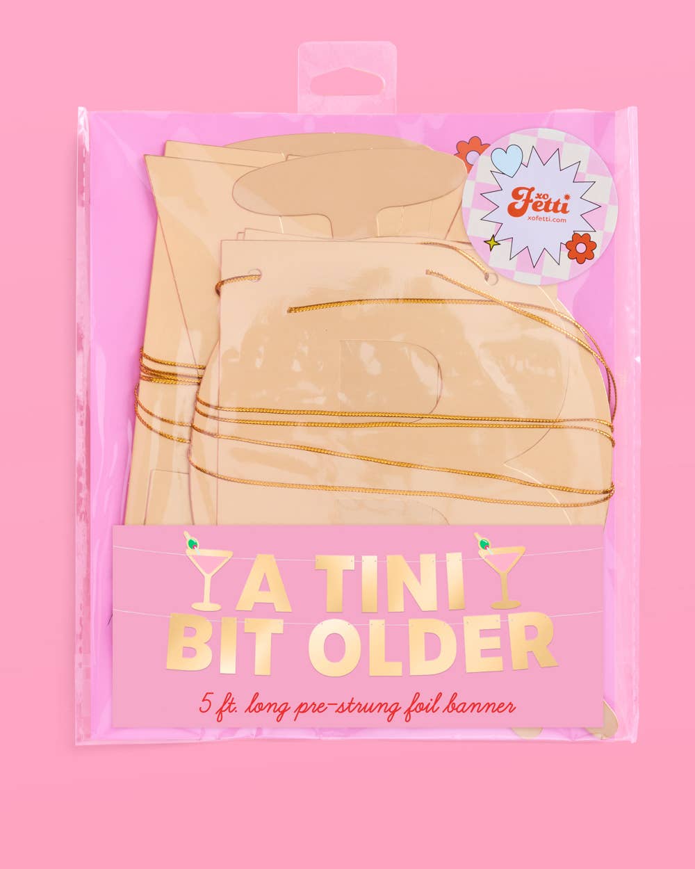 Packaged 'A Tini Bit Older' banner with gold accents on a pink background