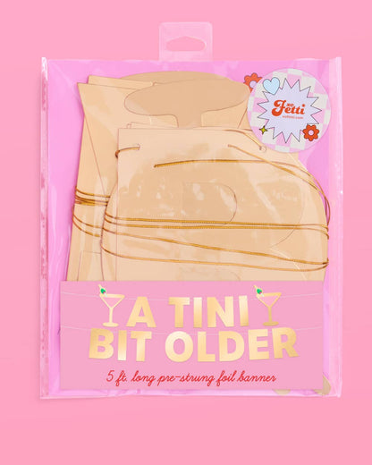 Packaged 'A Tini Bit Older' banner with gold accents on a pink background