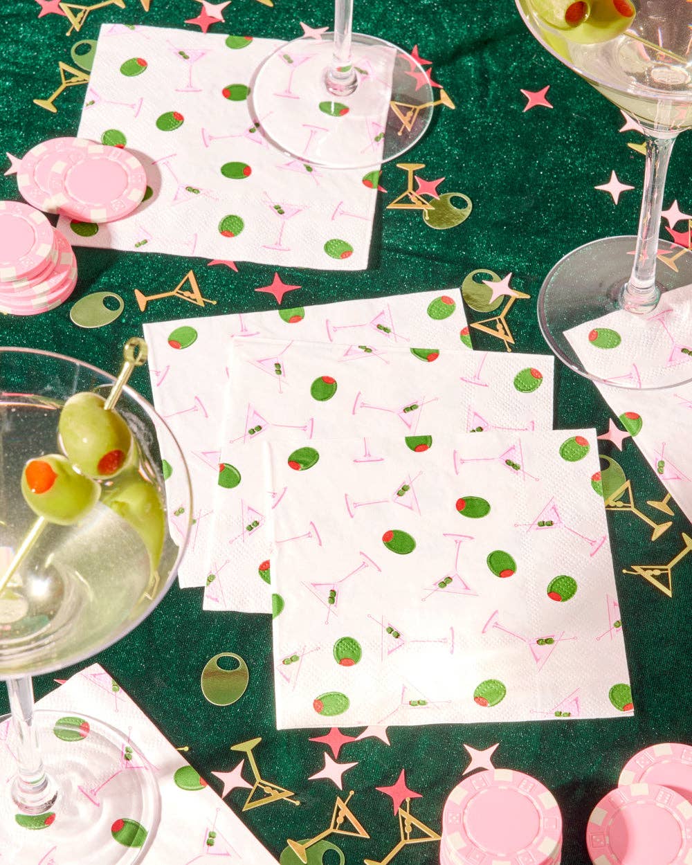 Table setting with cocktail-themed paper napkins and glasses on a green surface.