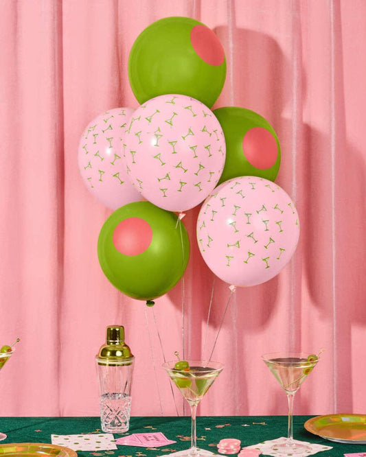 Decorative balloons with pink and green colors on a table against a pink curtain background.