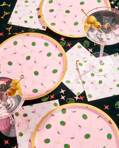 Party supplies with pink plates, napkins, and glasses featuring cocktail-themed designs.