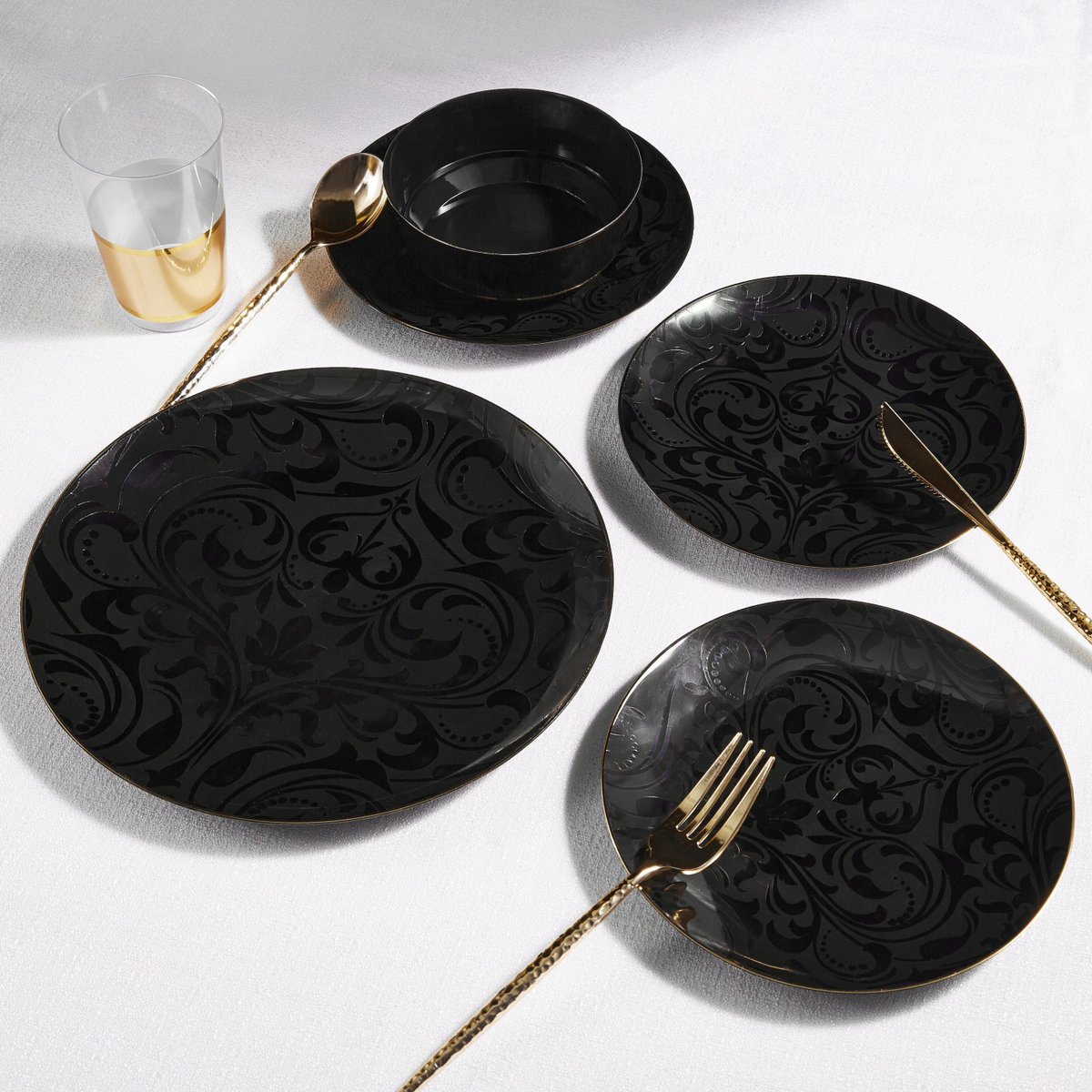 Black ornate plates with gold plastic cutlery on a white surface