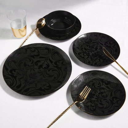 Black ornate plates with gold plastic cutlery on a white surface