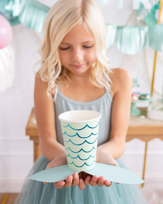 Young girl holding a paper cup with wave design to resemble a mermaid tail in a festive setting