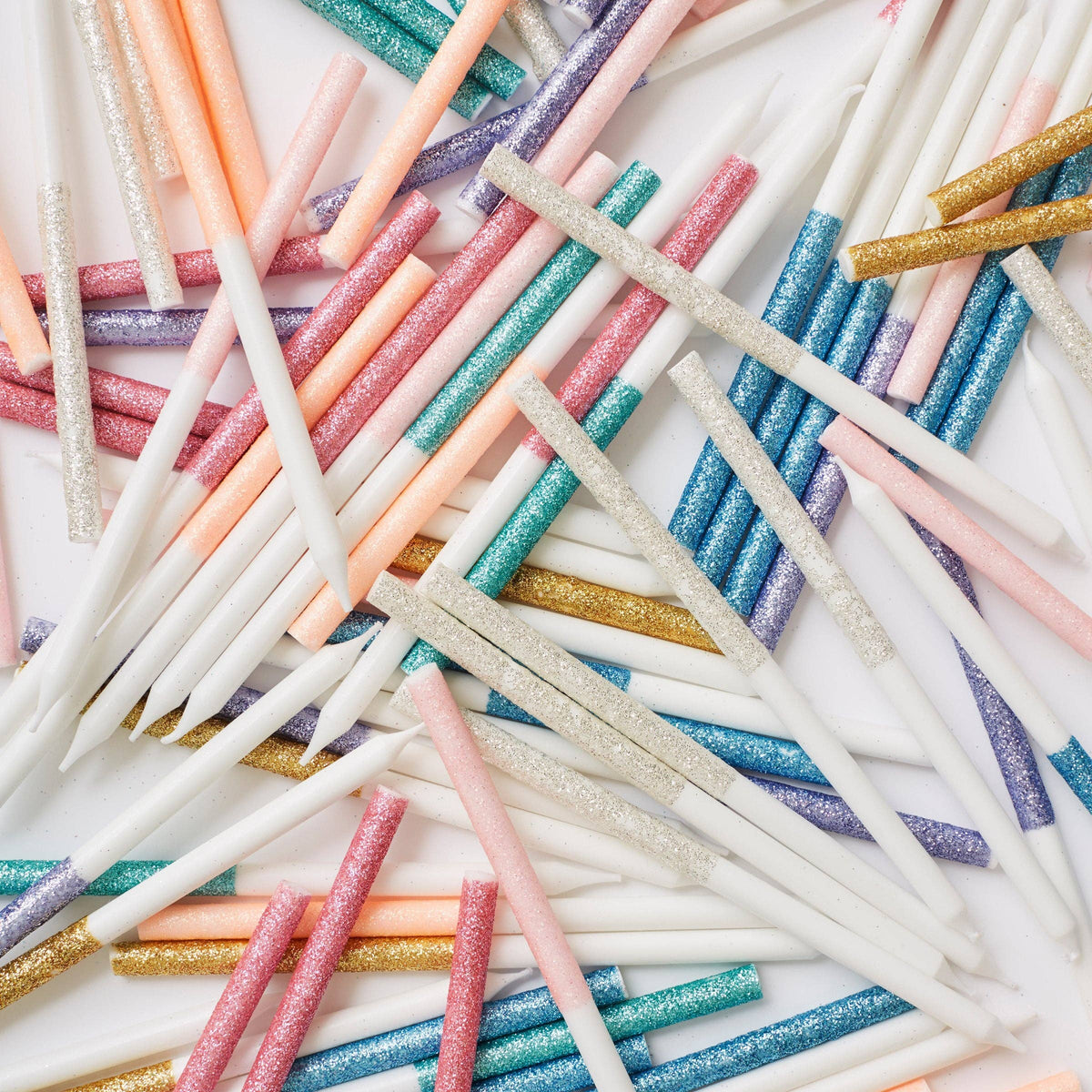 Colorful glittered birthday candles arranged in a pattern on a white background
