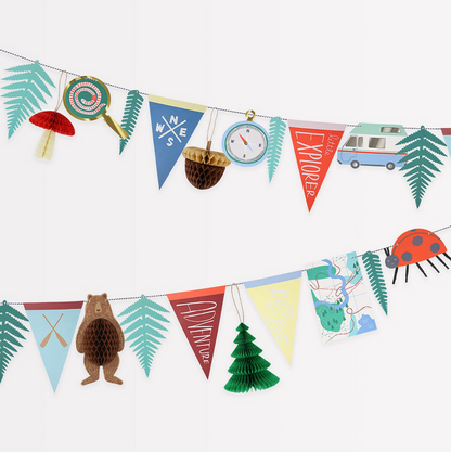 A colorful party garland with triangular pennants featuring camping-themed decorations such as a bear, camping hat, and trees, along with paper ferns, a honeycomb pattern, and a ladybug.