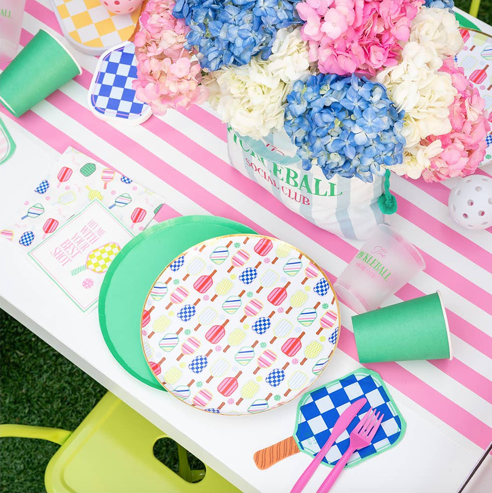 Colorful pickleball themed table setting with patterned plates, cups, and flowers on a striped table runner.
