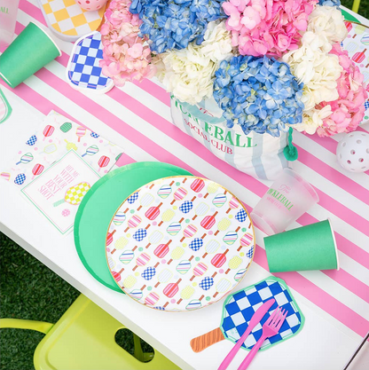 Colorful pickleball themed table setting with patterned plates, cups, and flowers on a striped table runner.