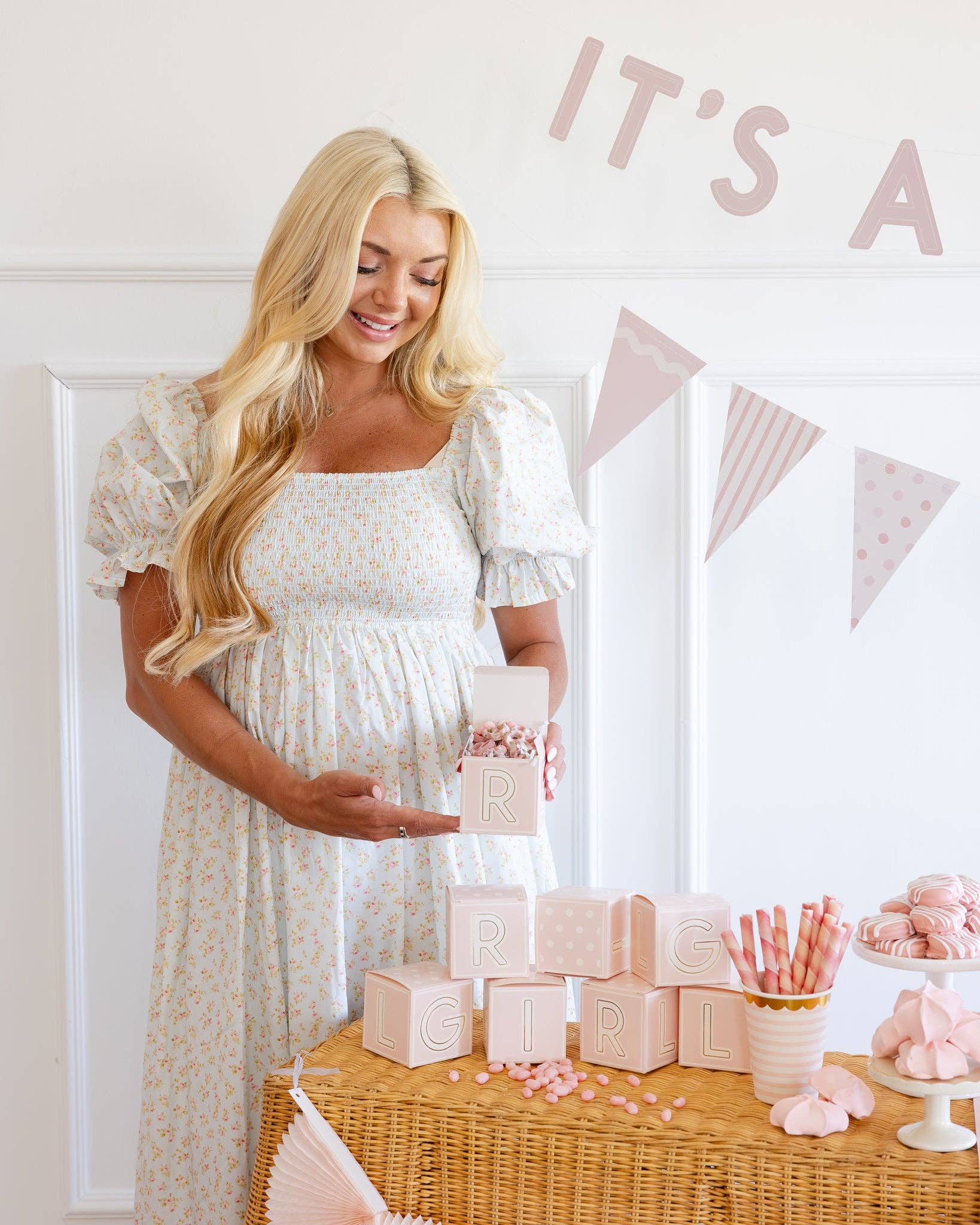 Pregnant woman at a baby shower with pink decorations and 'It's a girl' sign.