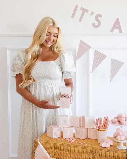 Pregnant woman at a baby shower with pink decorations and 'It's a girl' sign.