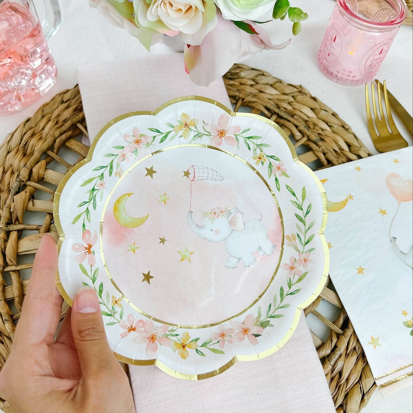 Pink and white decorative plate with elephant design held by a hand on a table setting.