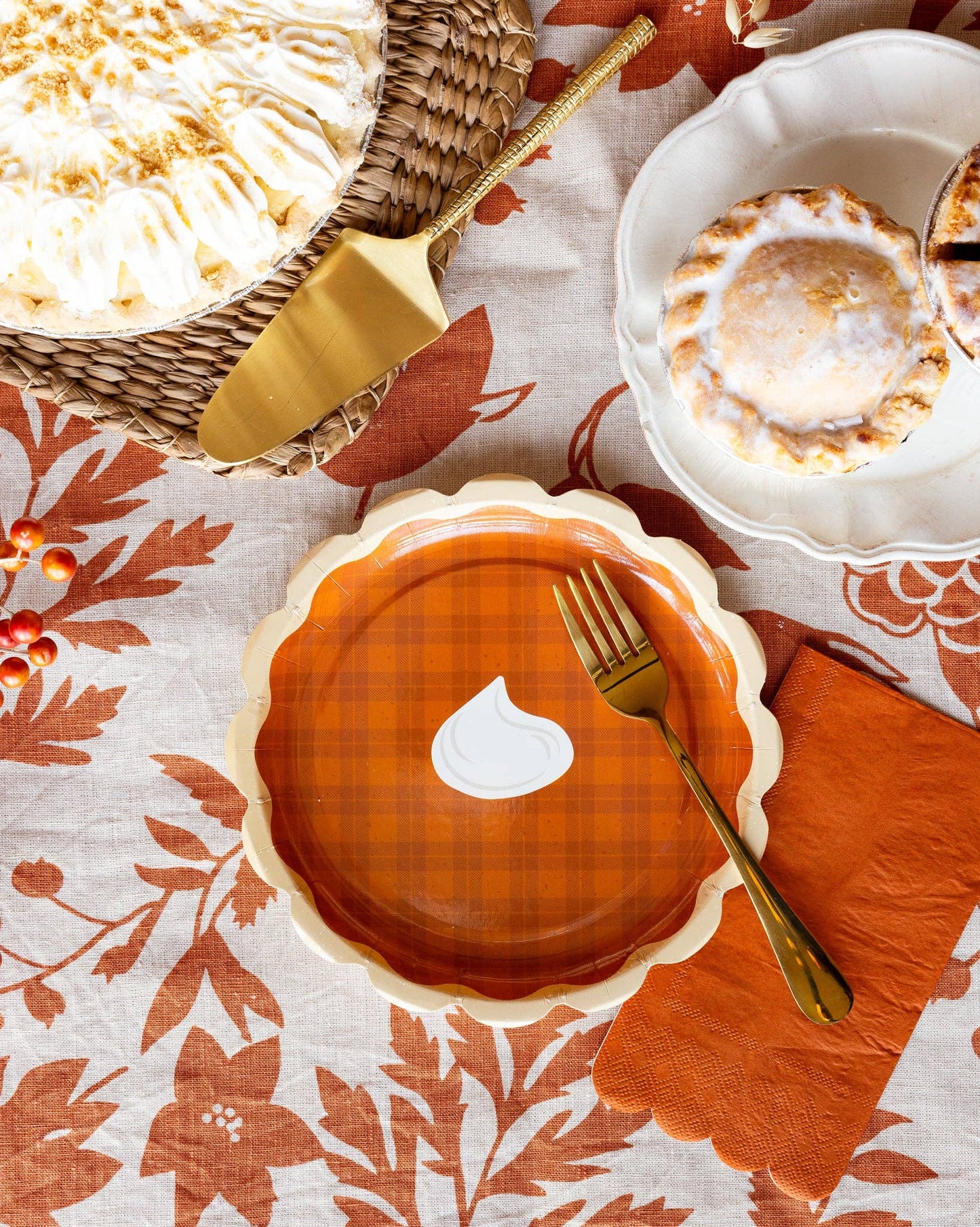 A decorative paper plate shaped like a plaid pumpkin pie on a with a gold fork on a patterned tablecloth.
