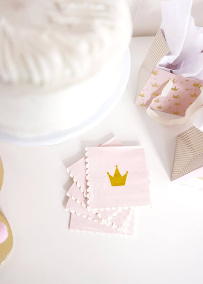 Pink cocktail napkins with gold crown design on a white surface.