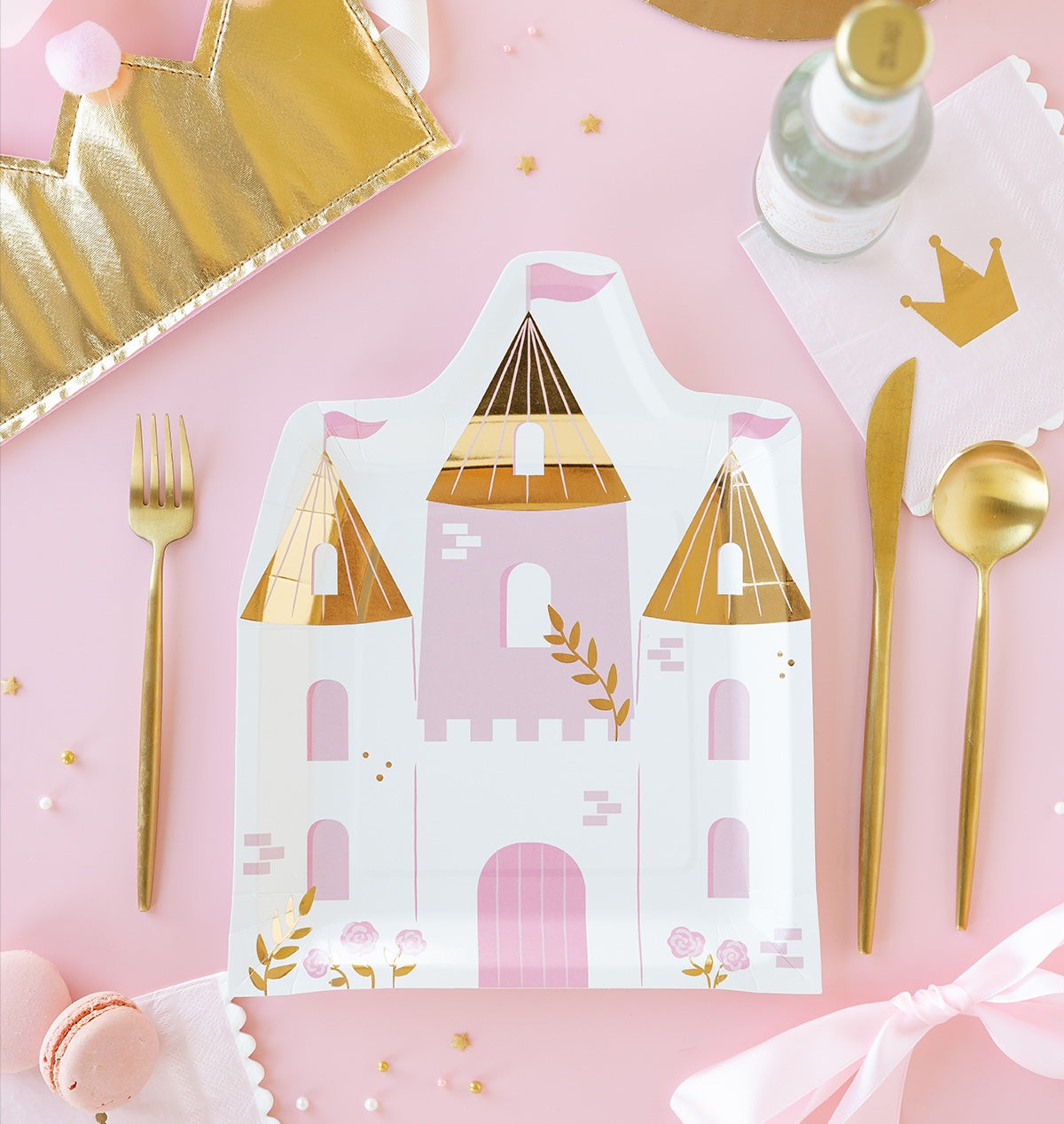 Paper party plates with castle design on a pink background with gold cutlery and decor.
