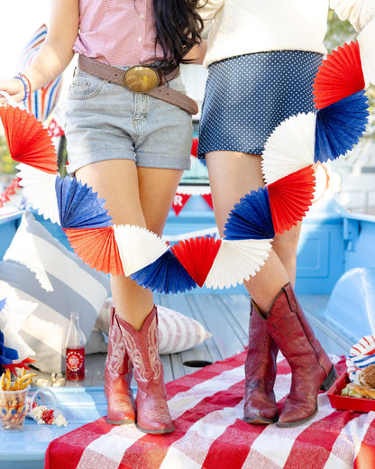 Two people wearing cowboy boots with a patriotic theme, standing on a red, white, and blue checkered blanket.