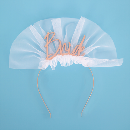 Rose Gold Metal Headband featuring Bride written in script on top with a short white tulle accent to resemble a bridal veil, set against a blue backdrop.