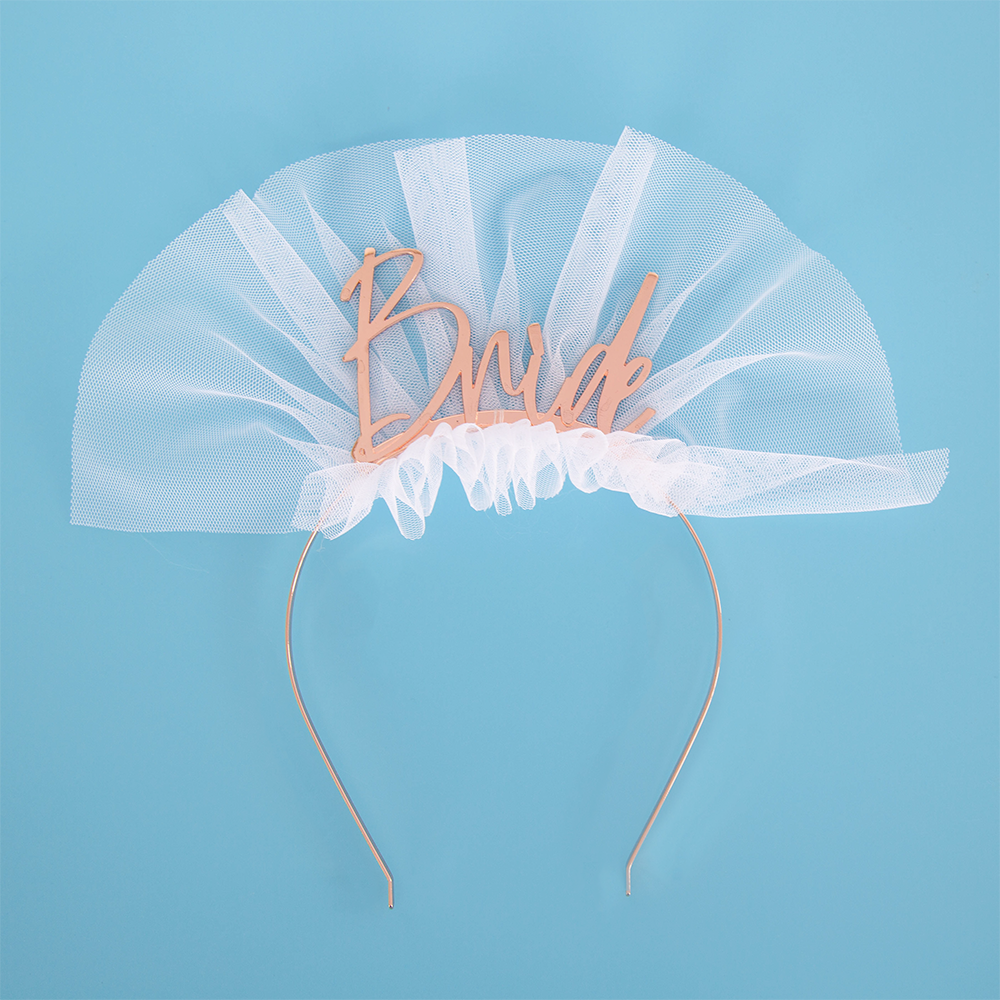 Rose Gold Metal Headband featuring Bride written in script on top with a short white tulle accent to resemble a bridal veil, set against a blue backdrop.