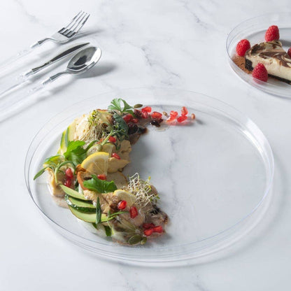 Delicate dish with garnishes on a clear plate, accompanied by a dessert with raspberries in the background.