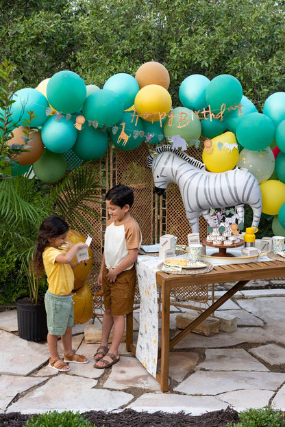 Children at a birthday party with balloons and a zebra balloon and safari themed cake toppers.