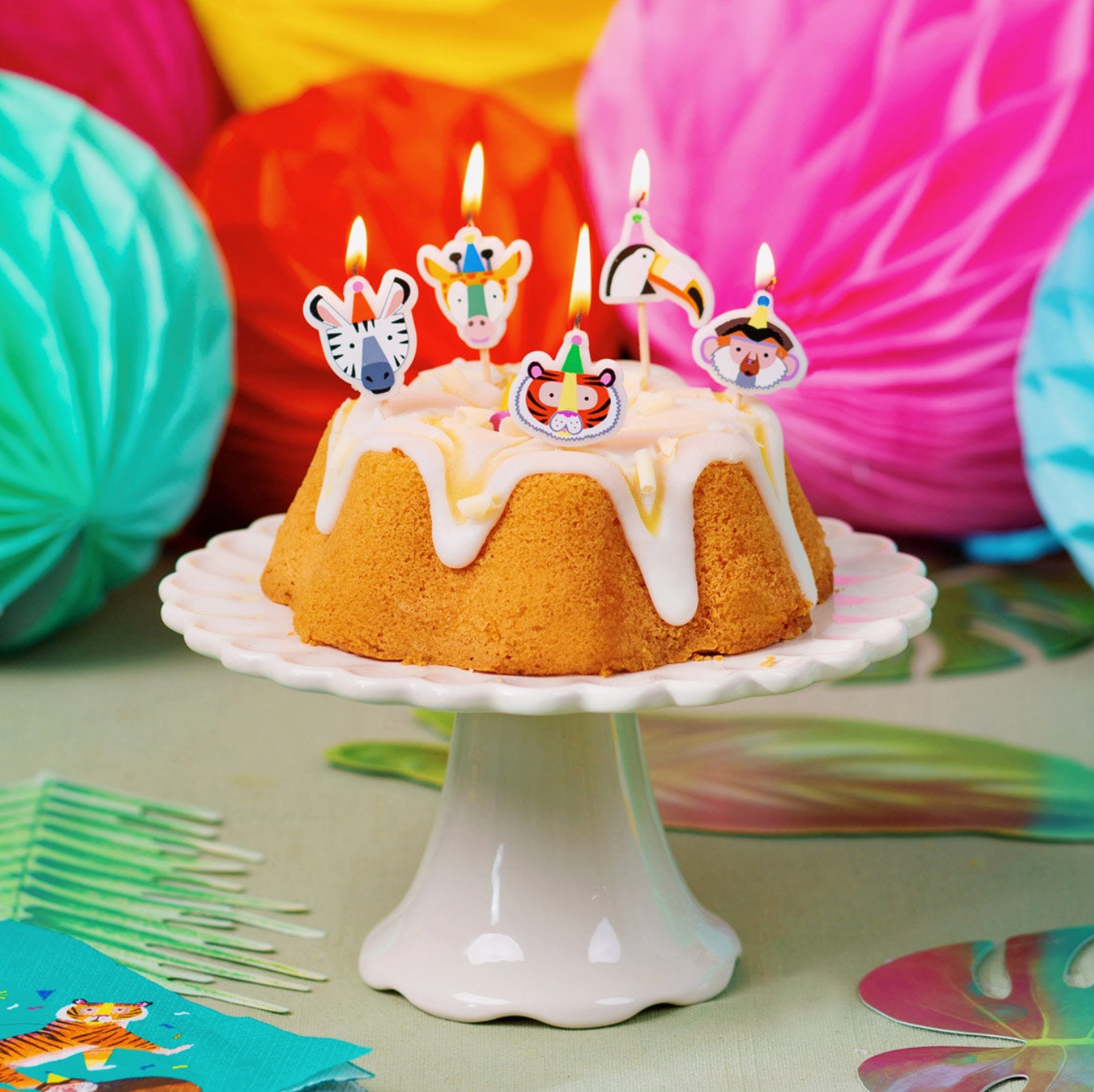 Small bundt cake with safari animal-themed candles on a white stand against a colorful background