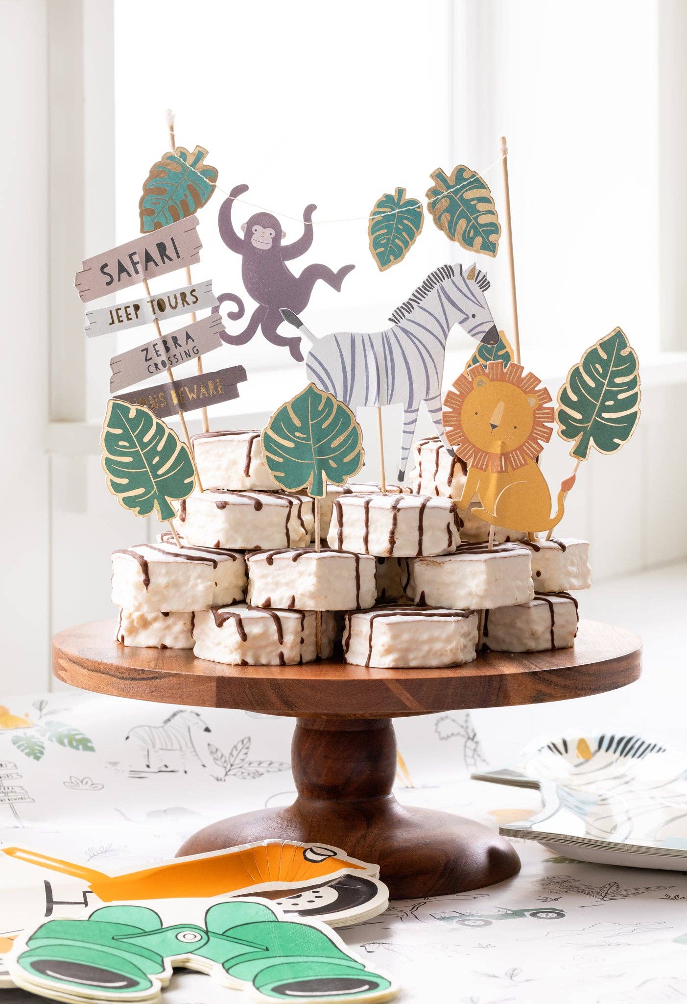 Decorative safari cake topper set with animals and leaves on a wooden stand.