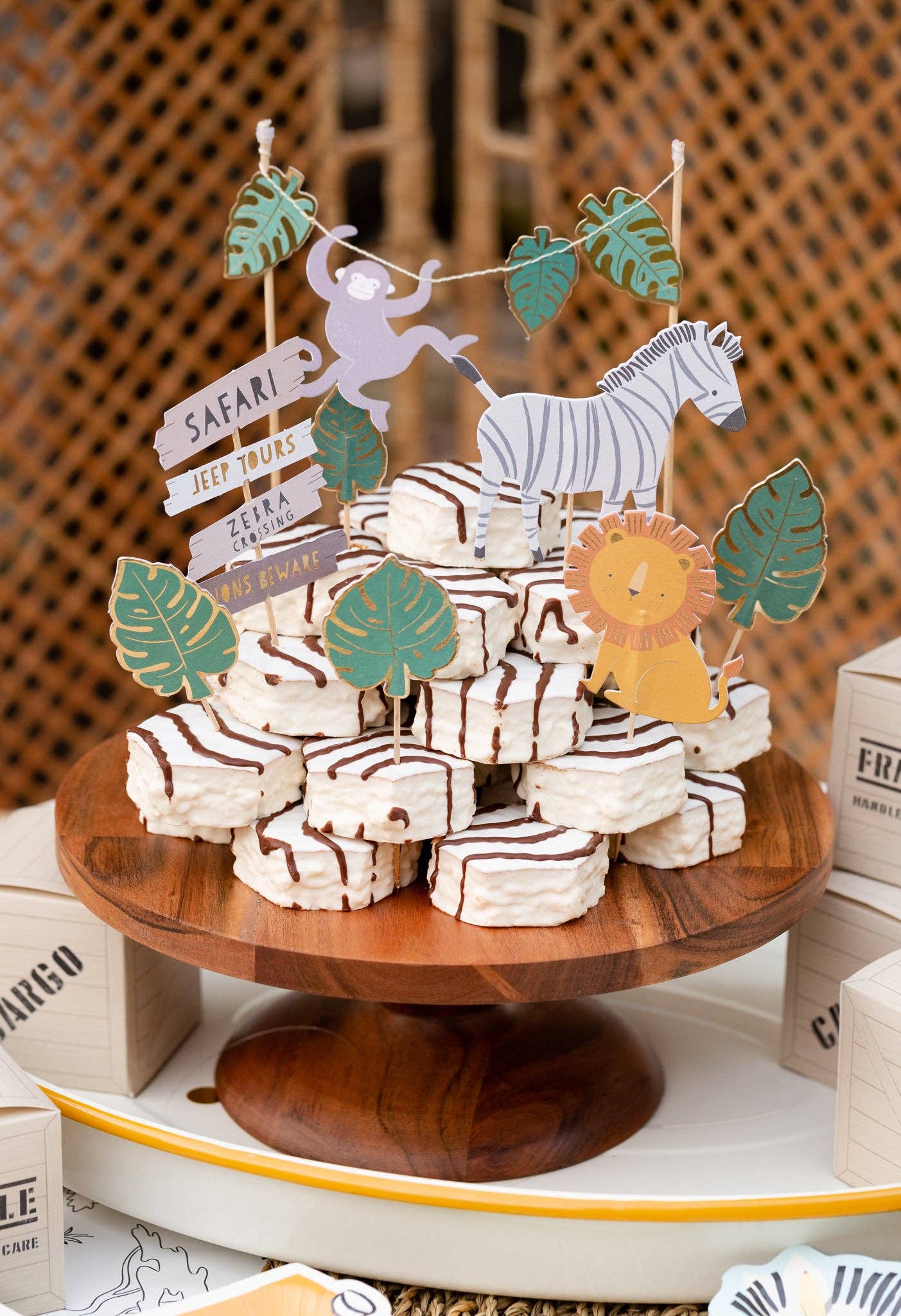 Wooden cake stand with safari animal-themed decorations and mini cakes against a woven background.