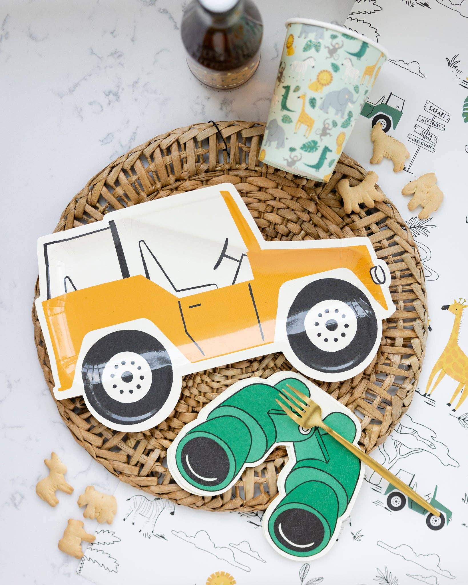 A set of binoculars shaped paper napkins with a safari animal theme, displayed on a woven mat alongside cookies and a fork.
