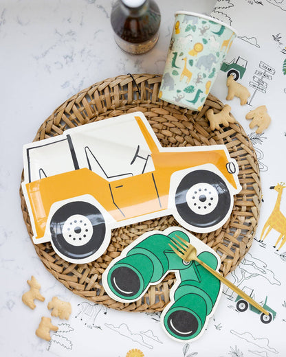 A set of binoculars shaped paper napkins with a safari animal theme, displayed on a woven mat alongside cookies and a fork.
