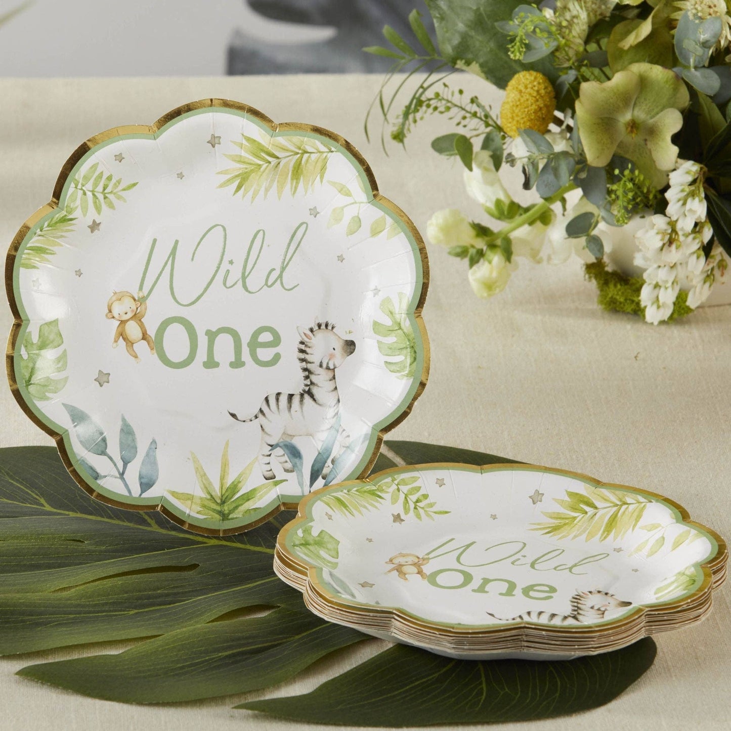Set of 'Wild One' small paper plates with safari animal illustrations on a table with flowers and leaves.
