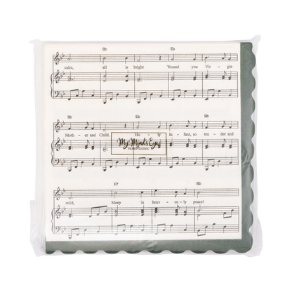 A square beverage napkin designed with sheet music print of "Silent Night" with a scalloped dark green border in clear plastic packaging.