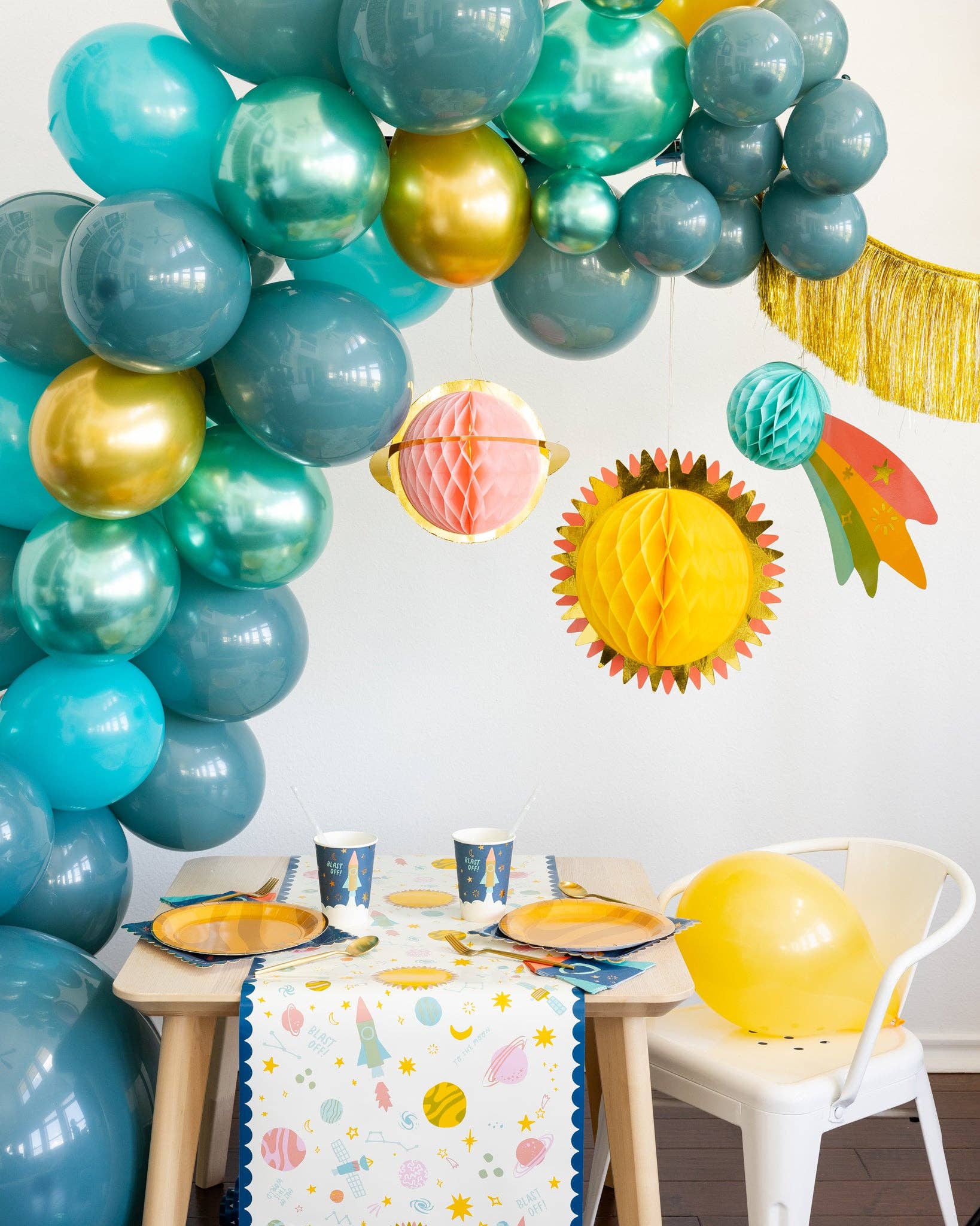 Colorful balloon arch with hanging planet decorations over a table set for a space themed party.
