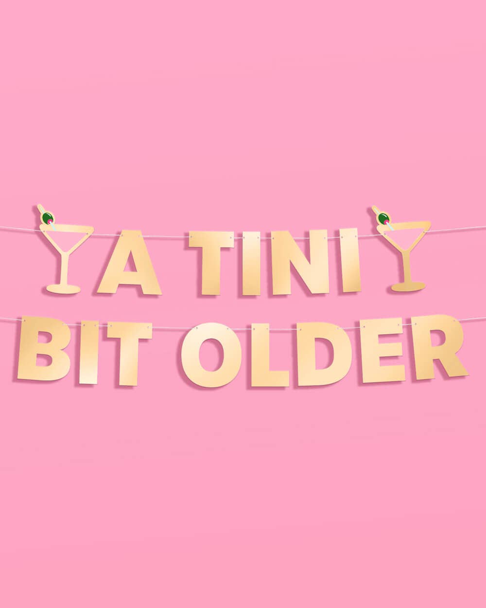 Gold 'A TINI Bit Older' banner with cocktail glasses on a pink background