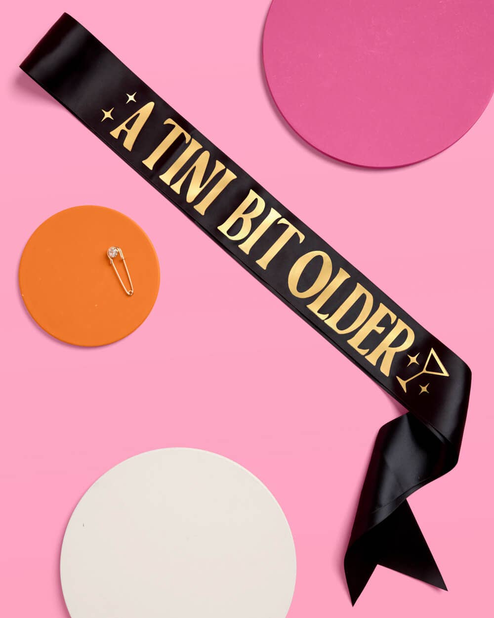 Black sash with 'A TINI BIT OLDER' text on a pink background