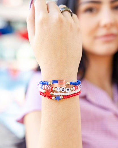 Person wearing a set of colorful beaded bracelets with 'USA' on a blurred background
