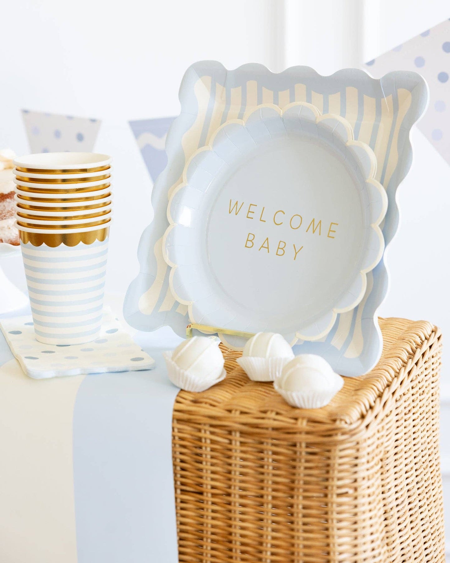 Decorative baby shower plate with 'Welcome Baby' text on a table with white cups and decorative elements.