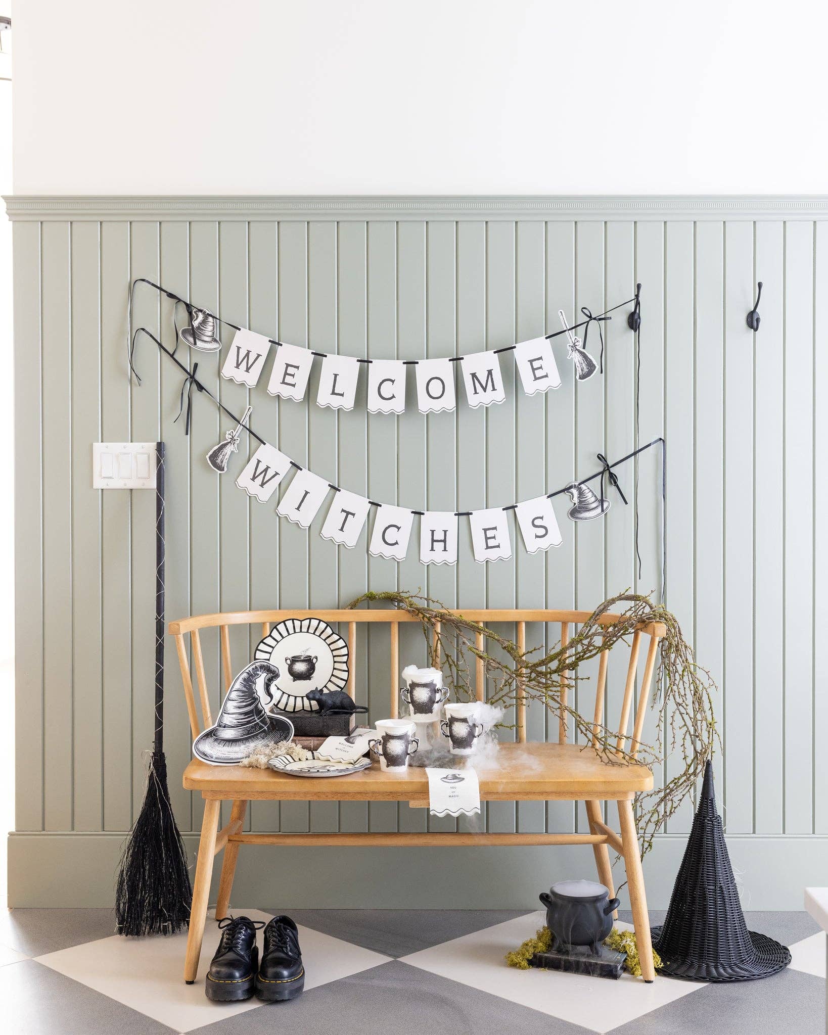 Halloween-themed decor with a 'Welcome Witches' banner, broom, and cauldron on a wooden bench.