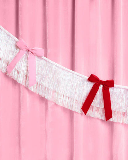 White iridescent fringe garland with pink and red bows on a pink background.